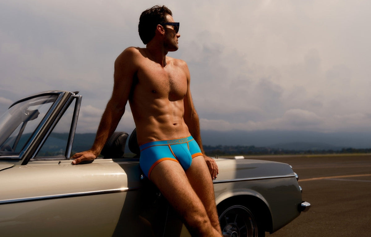 Lifestyle editorial image featuring a male model wearing Cocksox CX68N Apex Collection men's underwear trunks in Capri while leaning back against a classic car